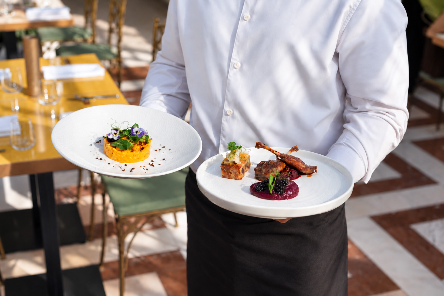 Číšník Villa Richter Restaurant servíruje dva talíře – dýňové rizoto s jedlými květy a kachní stehýnko s ostružinami